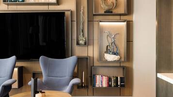 A modern living room with a large flat-screen TV, two armchairs, a coffee table, and a bookshelf with books.