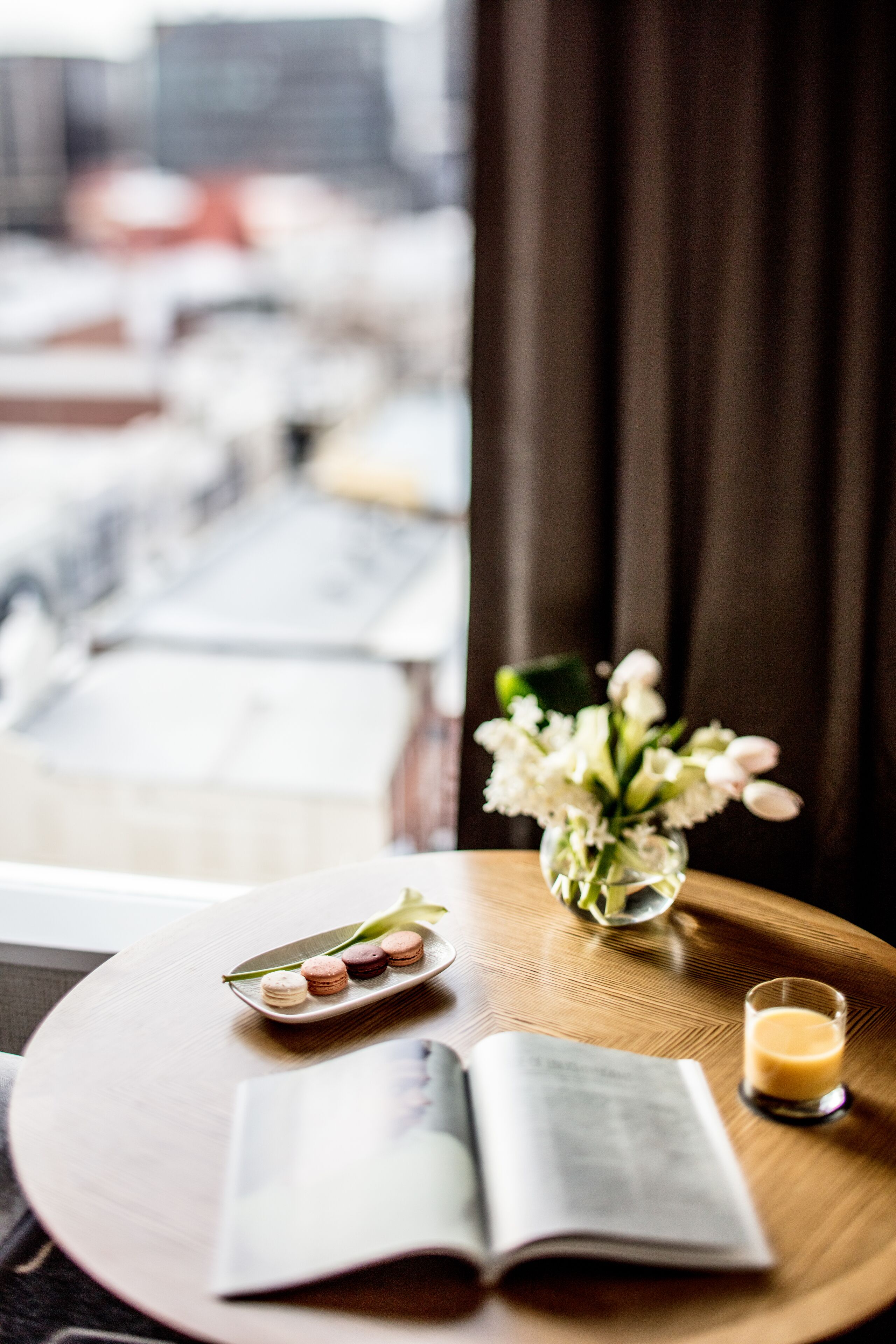 A wooden table with a book, a glass of drink, and a plate of macarons.