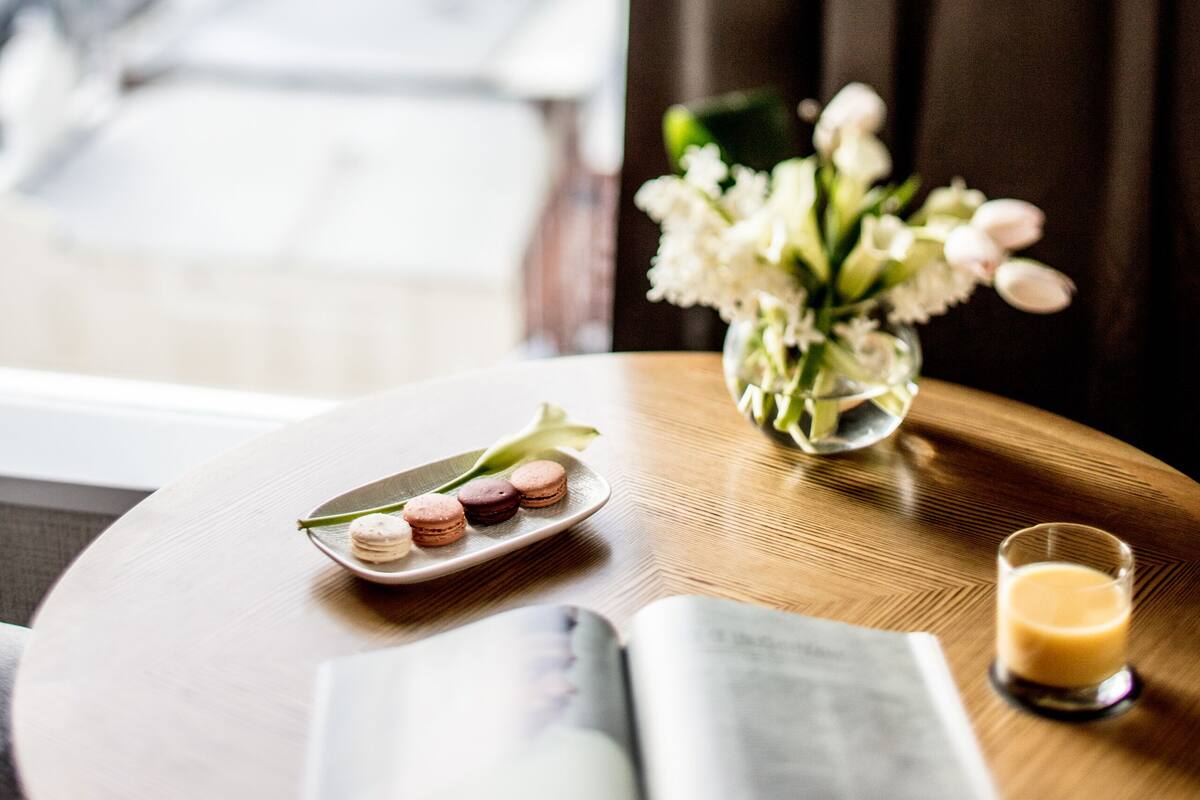 A wooden table with a book, a glass of drink, and a plate of macarons.