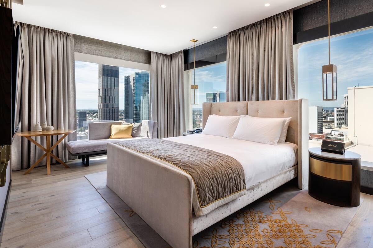 A modern hotel room with a large bed, a sofa, a small table, and a view of the cityscape.