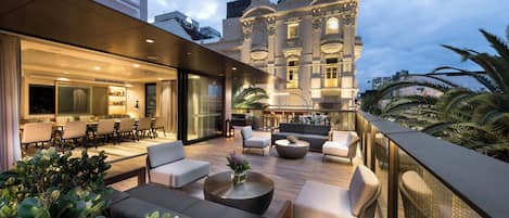 Un salón en la azotea con asientos al aire libre, zona de comedor y vistas a un edificio histórico.