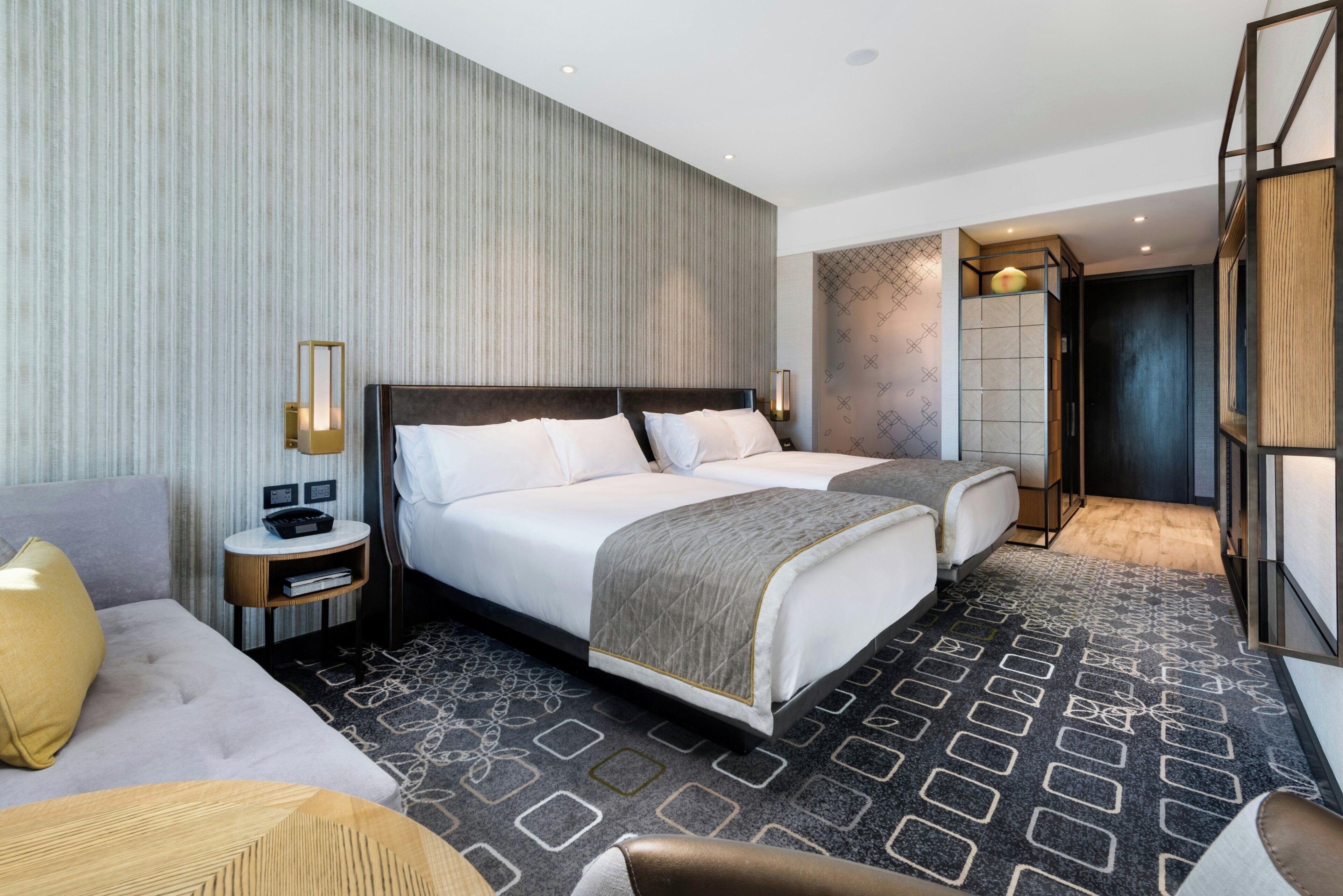 A modern hotel room with a large bed, a sofa, a desk, and a wardrobe.