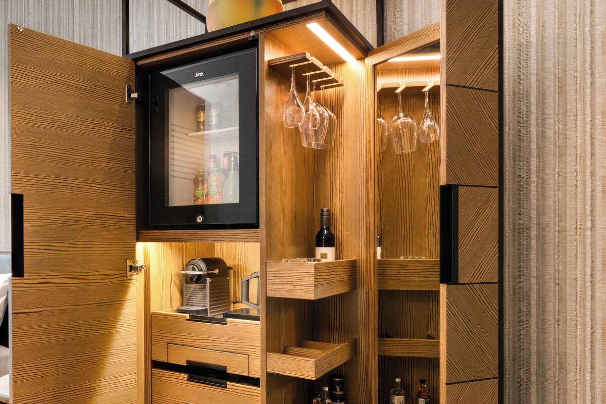 A modern kitchen with wooden cabinetry, a built-in wine cooler, and wine glasses hanging on a rack.