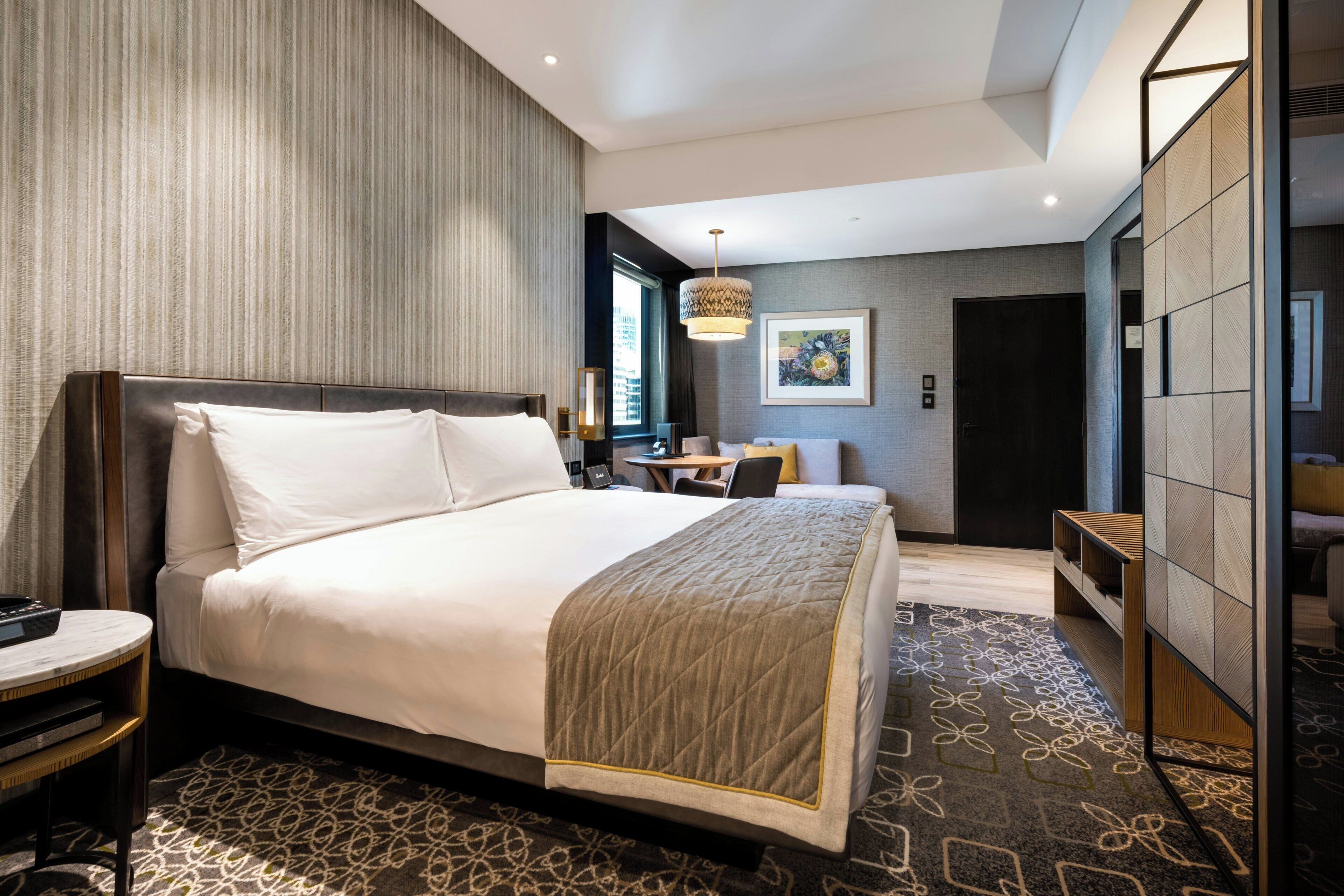 A modern hotel room with a large bed, a desk, and a seating area.