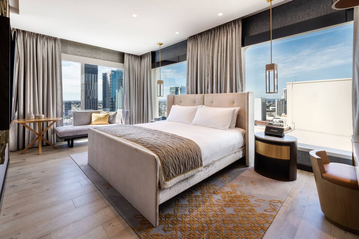 A modern hotel room with a large bed, a seating area, and a view of the cityscape.