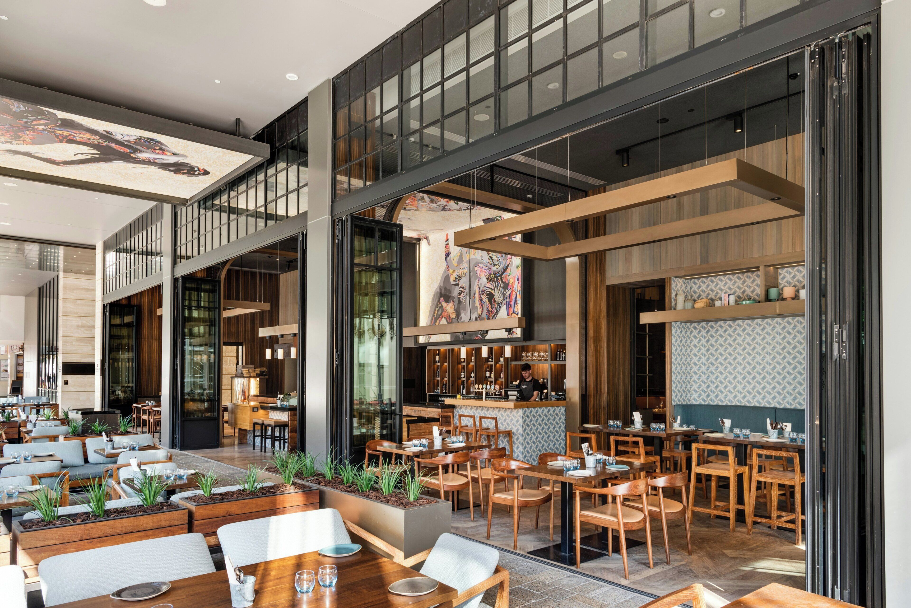 A modern restaurant with multiple dining areas, a bar, and a visible kitchen.