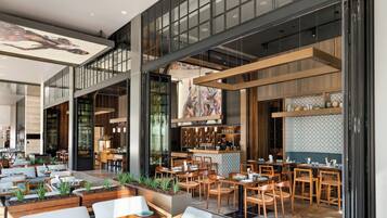 A modern restaurant with multiple dining areas, a bar, and a visible kitchen.