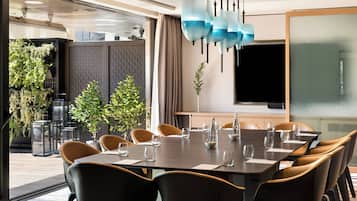 A modern conference room with a long table, chairs, and a large screen.
