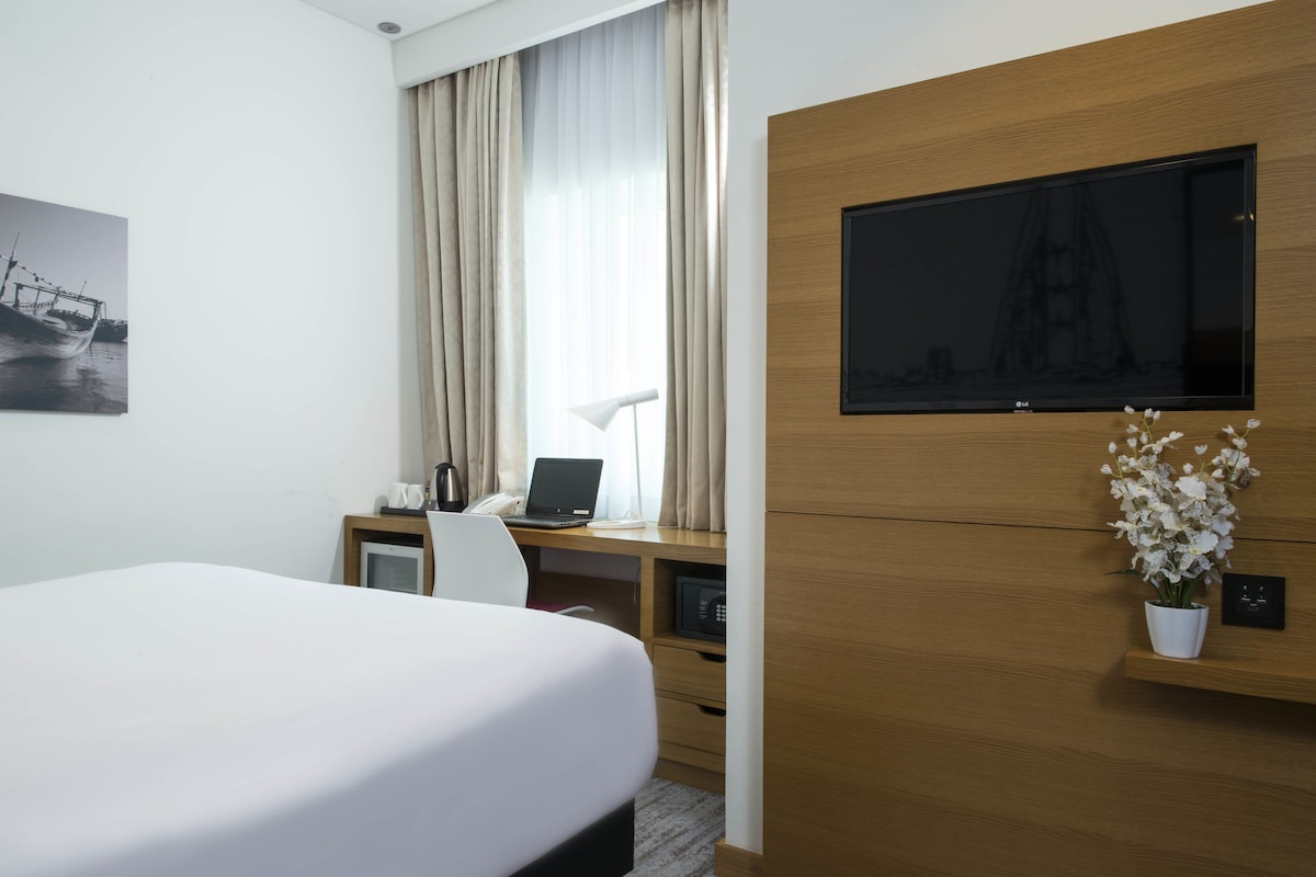 Una habitación de hotel con cama, escritorio, laptop, televisor y una pequeña planta en maceta.