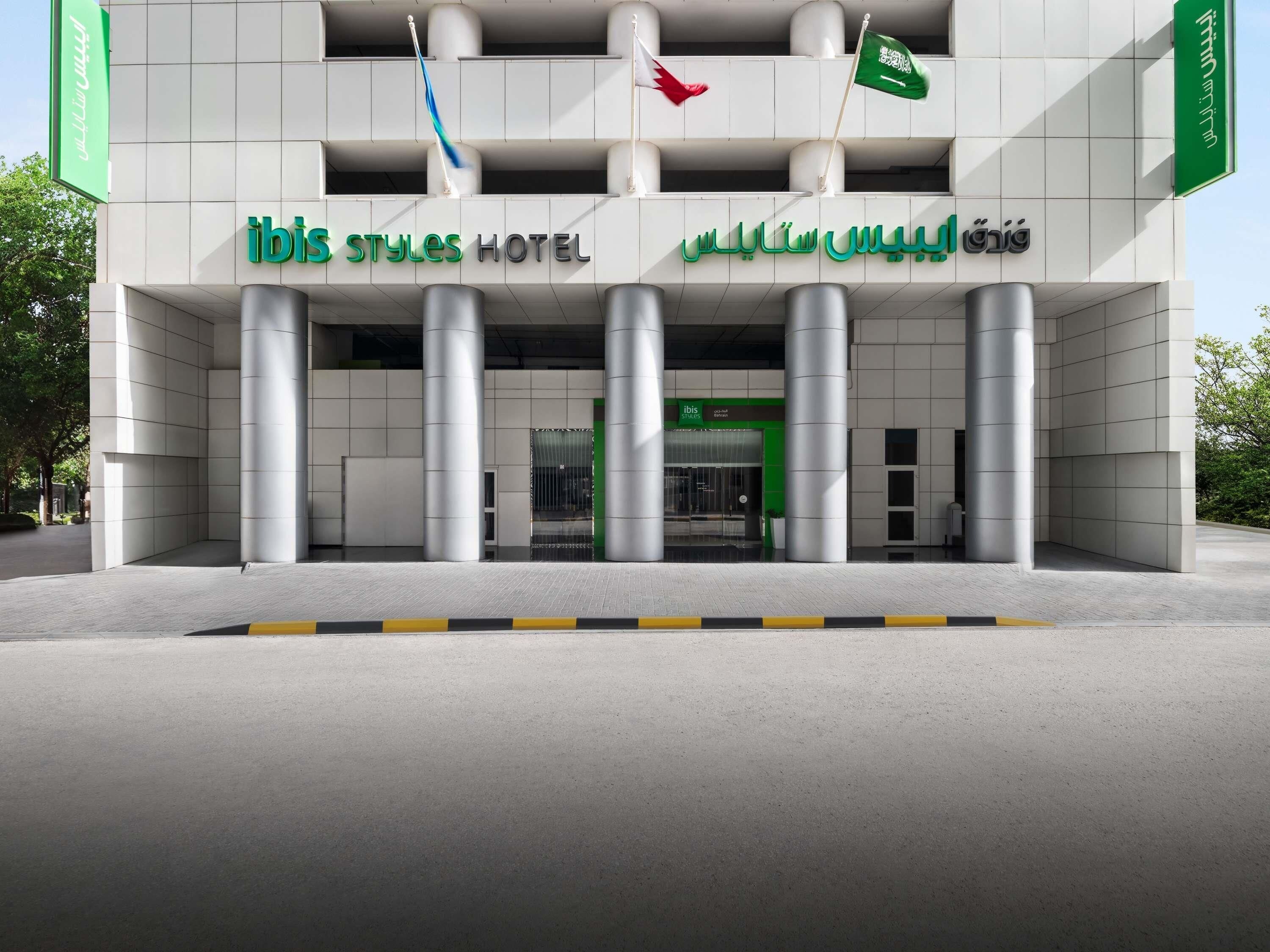 A modern hotel entrance with a prominent sign, large pillars, and flags.