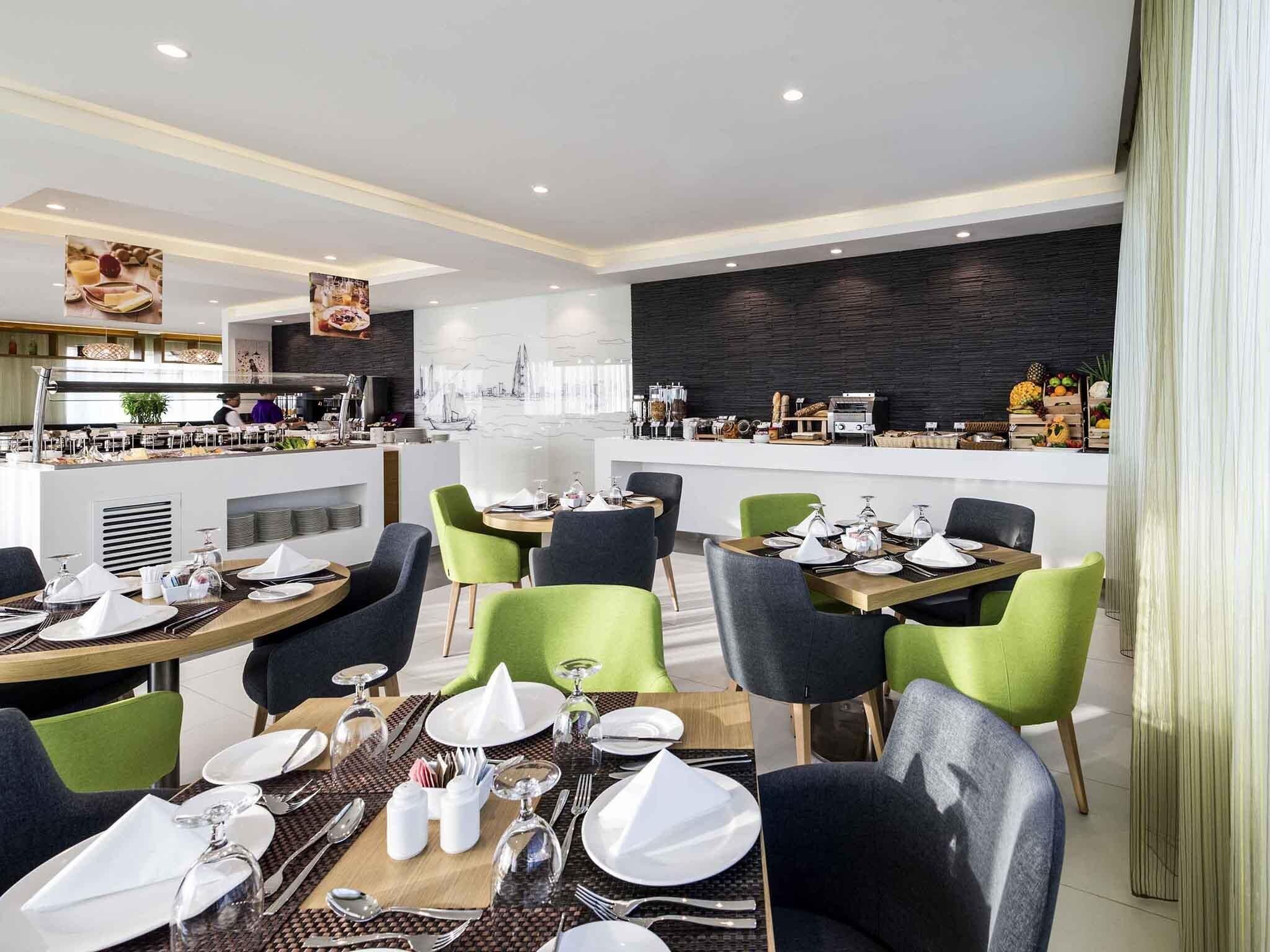 Un espace repas moderne avec des tables rondes, des chaises vertes et noires, et un buffet en arrière-plan.