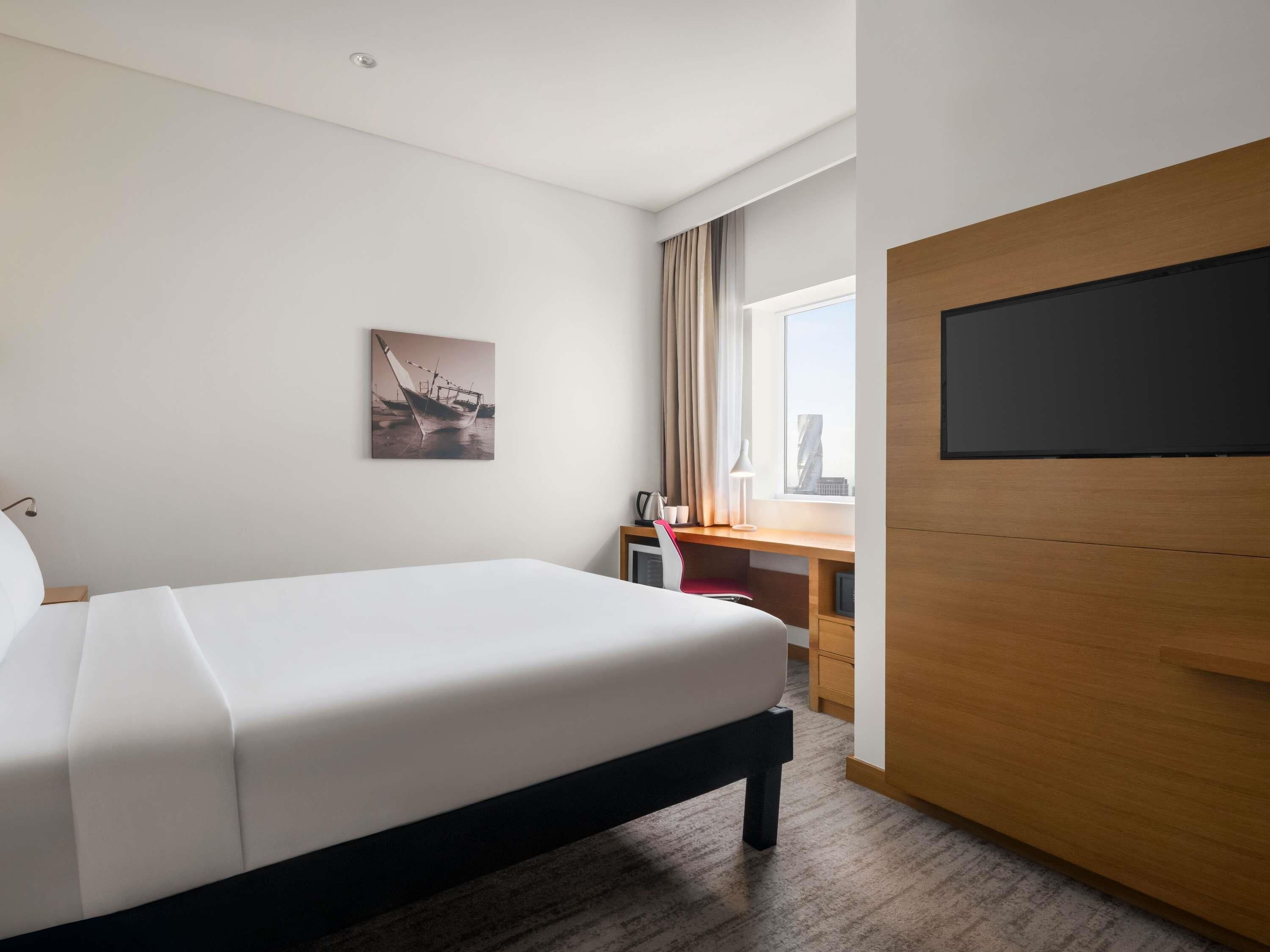 Una camera d'albergo con un letto, una scrivania, una sedia, una televisione e una finestra con tende.