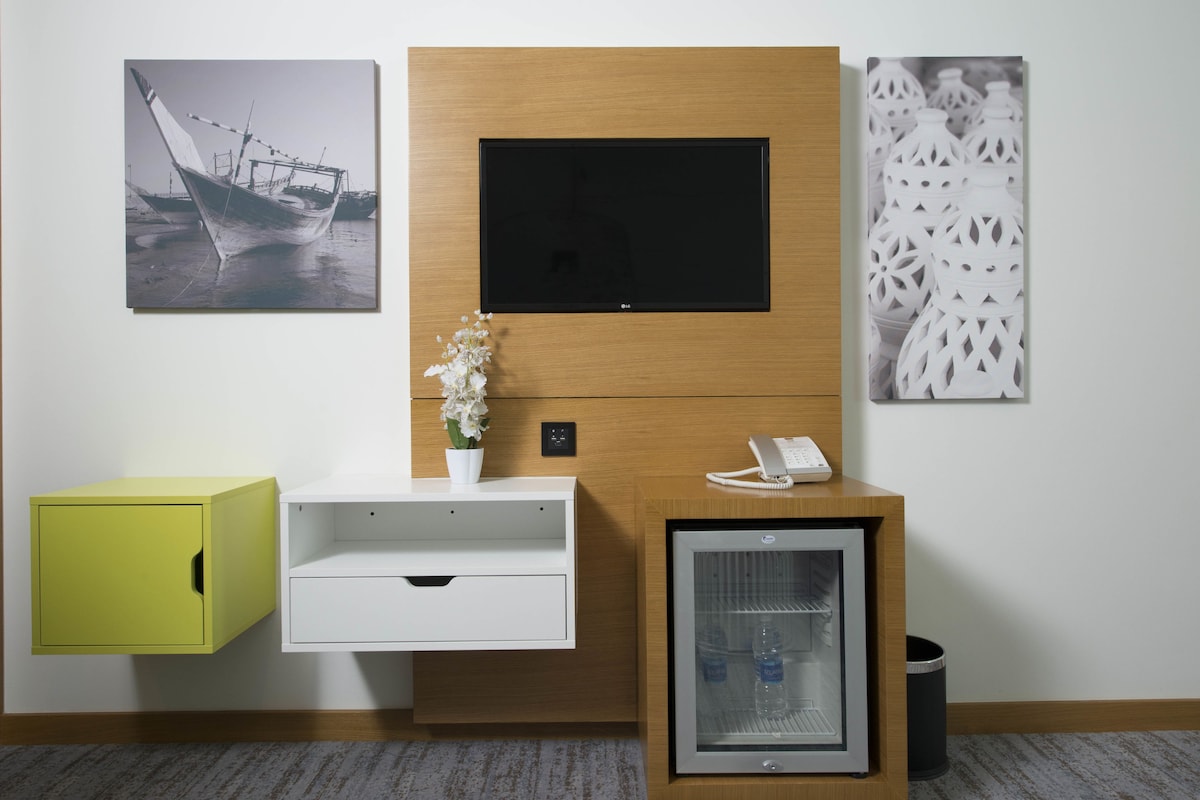 Un mostrador de recepción con un televisor de pantalla plana, un refrigerador pequeño, un teléfono y un armario amarillo.