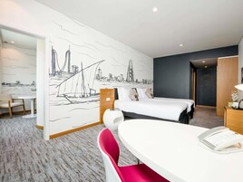 Habitación de hotel con cama, escritorio, silla y un mural en la pared que representa un paisaje urbano.