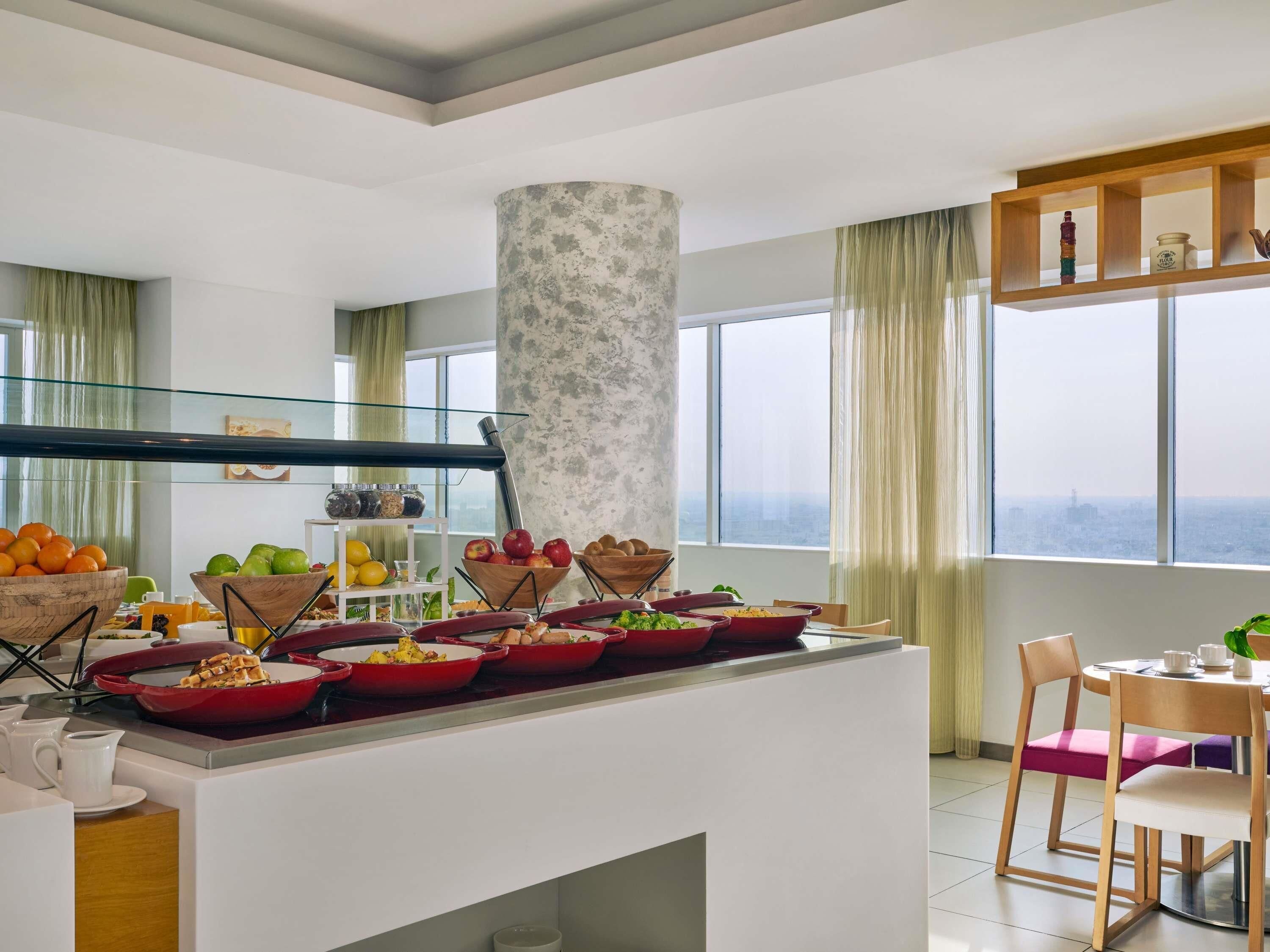 A modern kitchen with a central island, various food items, and a view of the city.