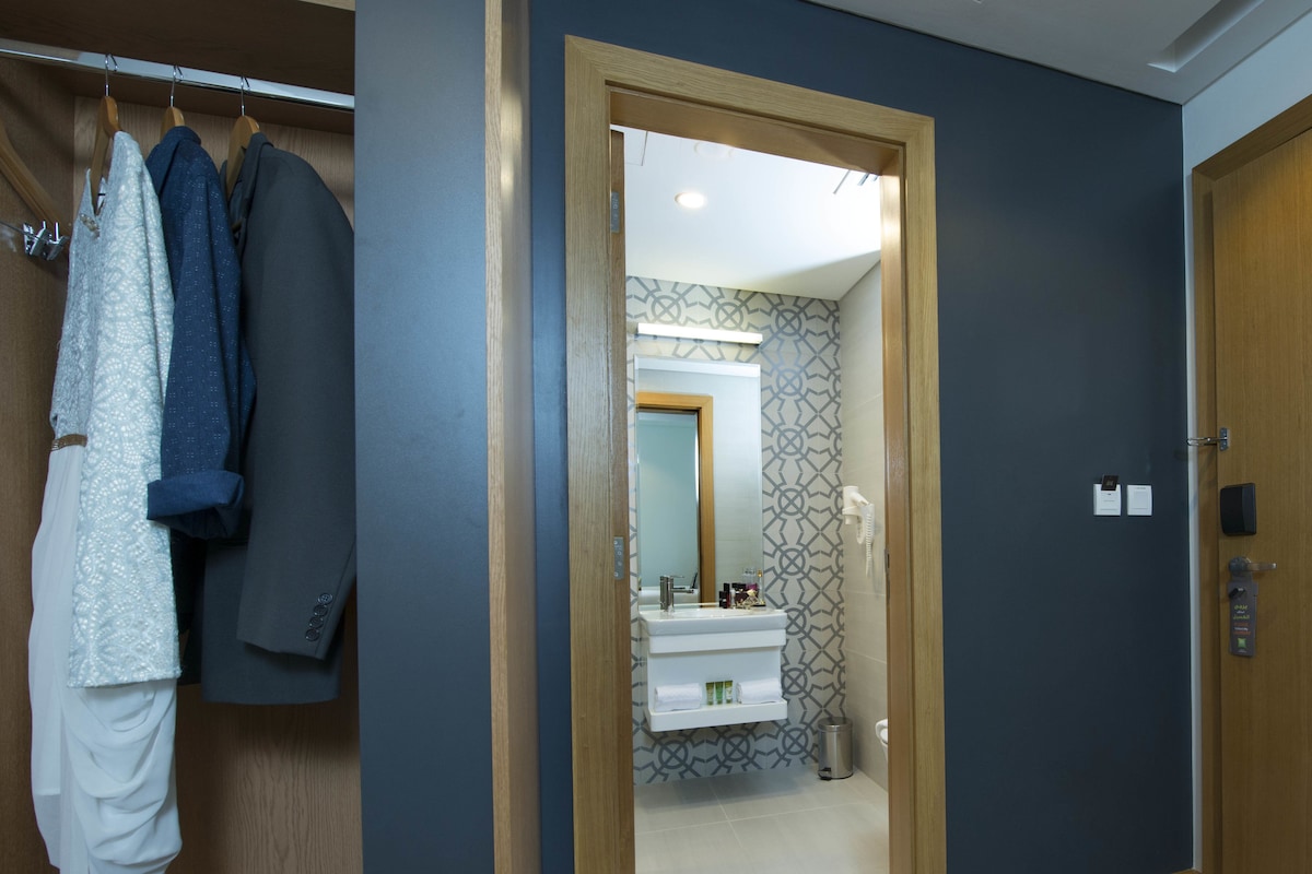 Pasillo que conduce a un baño con espejo, lavamanos y pared con diseño.