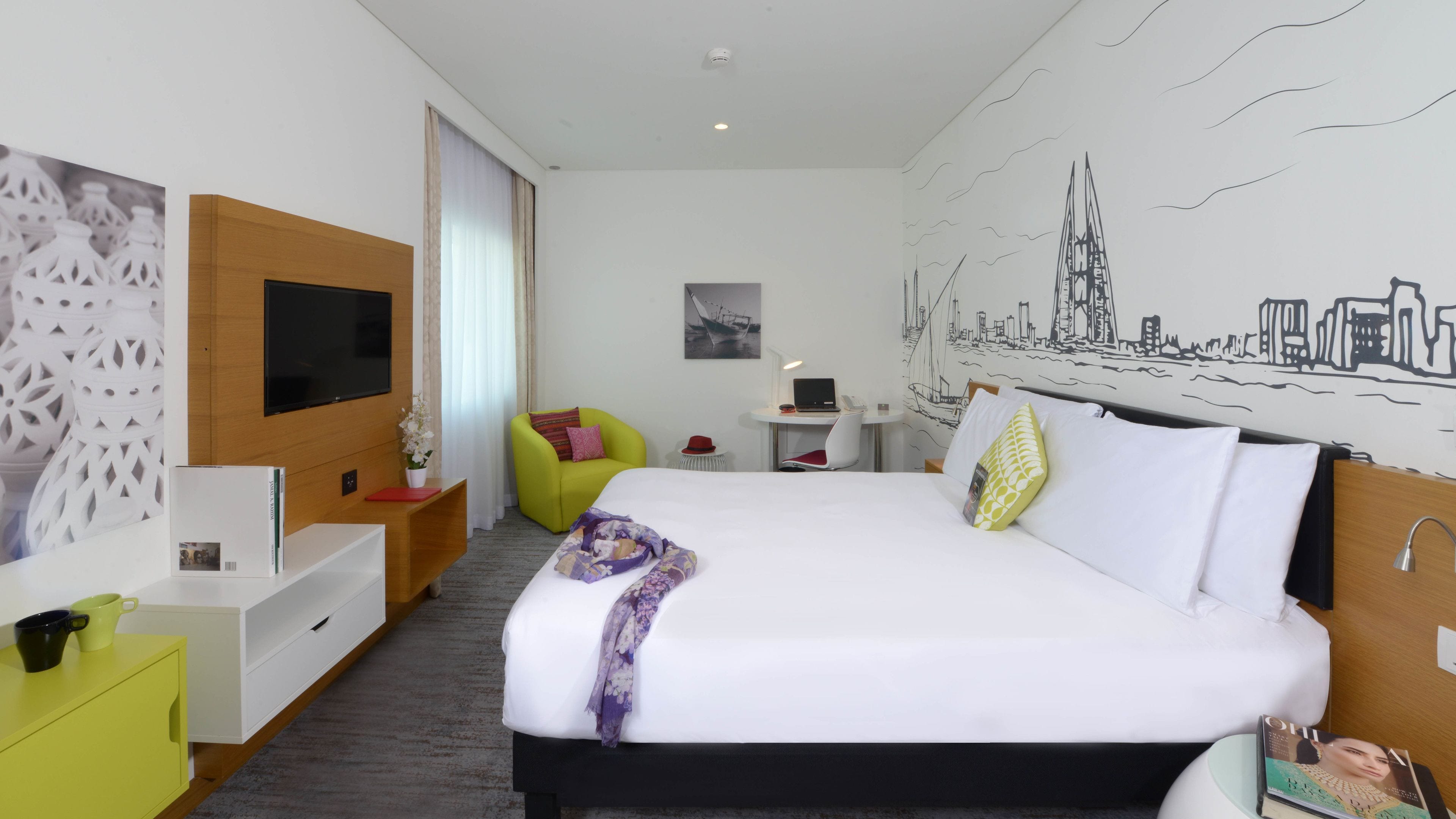 Habitación de hotel con cama, escritorio, silla, televisor y un mural en la pared.
