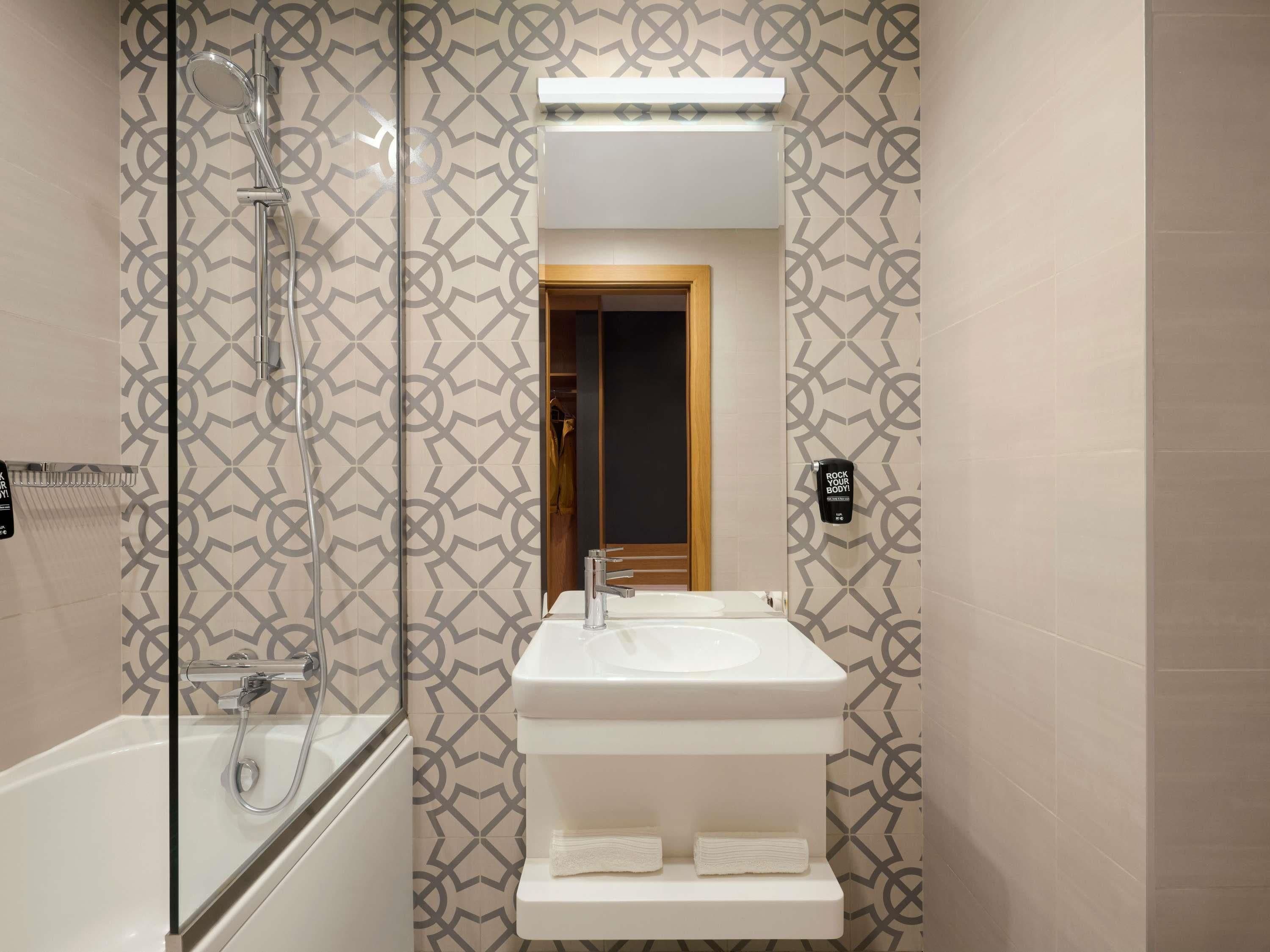 A modern bathroom with a glass-enclosed shower, a white sink with a mirror above it, and patterned wall tiles.