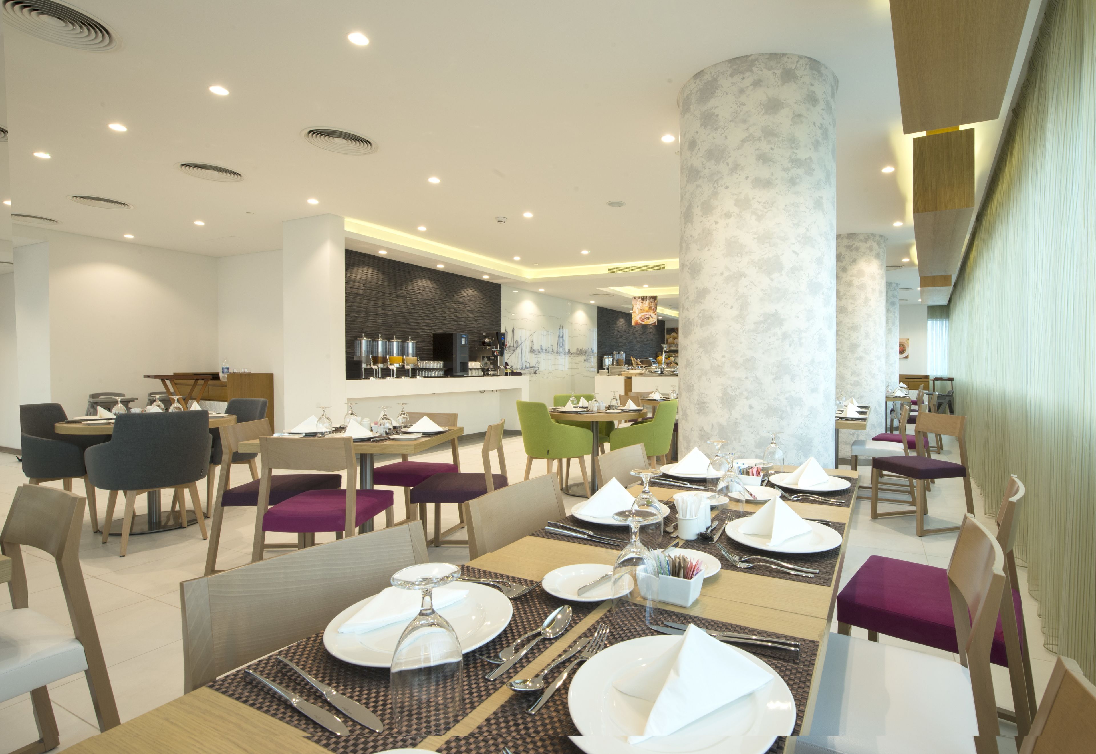 Un espace de restauration moderne avec des tables dressées pour le service, un bar et une vue sur les gratte-ciel de la ville.