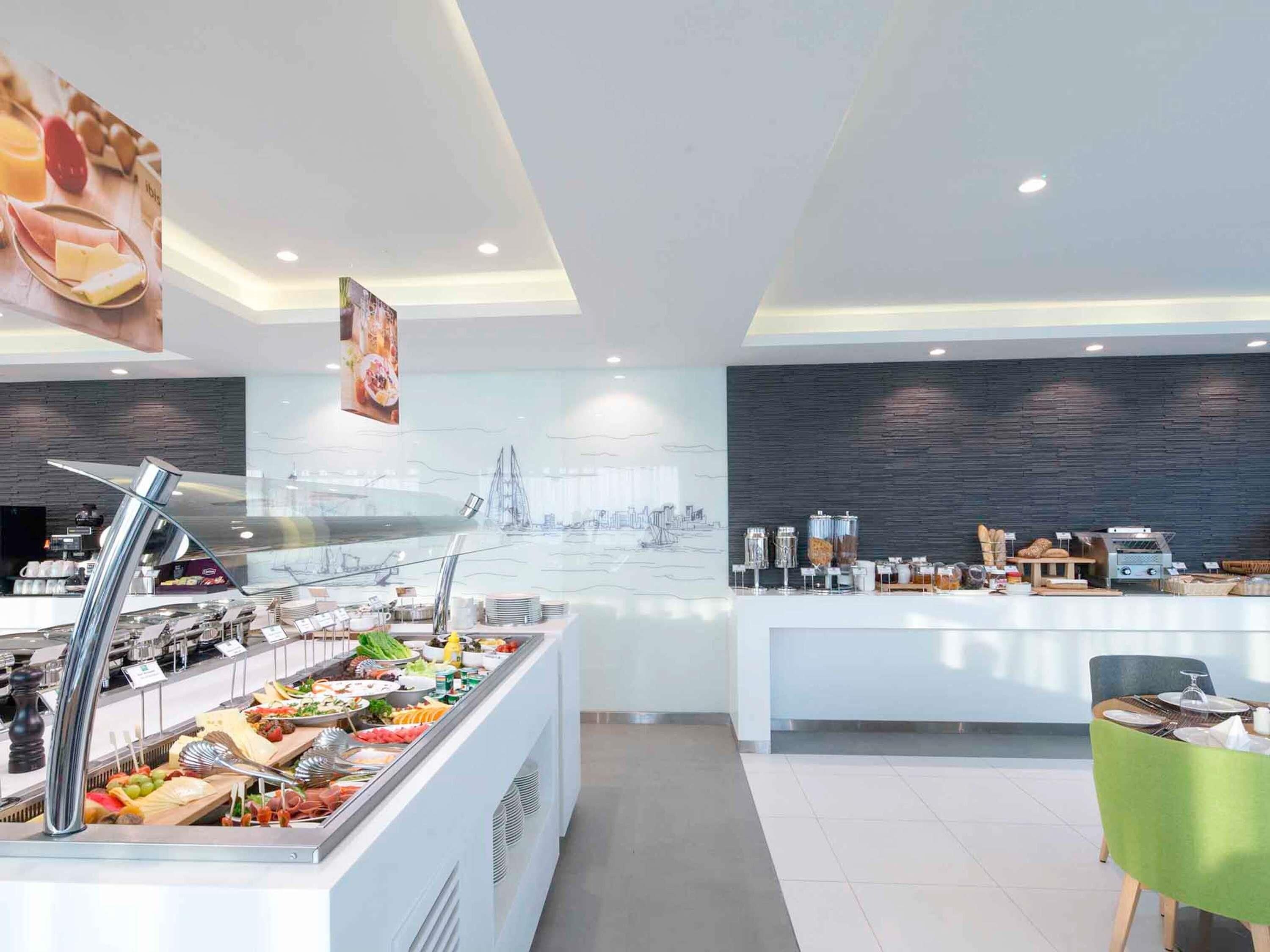 Una moderna colazione a buffet con diverse opzioni gastronomiche, un angolo caffè e un'area salotto con una sedia verde.