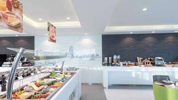 A modern breakfast bar with a variety of food options, a coffee station, and a seating area with a green chair.