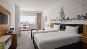 A hotel room with two beds, a desk with a chair, a TV, and a cityscape mural on the wall. - ibis Styles Manama Diplomatic Area (Manama)