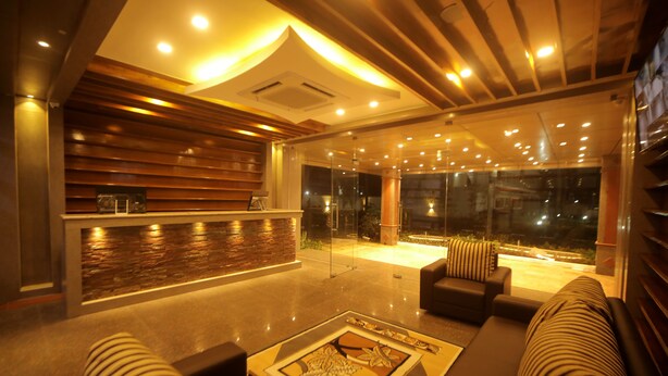 A modern lobby with a reception desk, seating area, and large windows. - Lee Crysstal (Tirupporur)