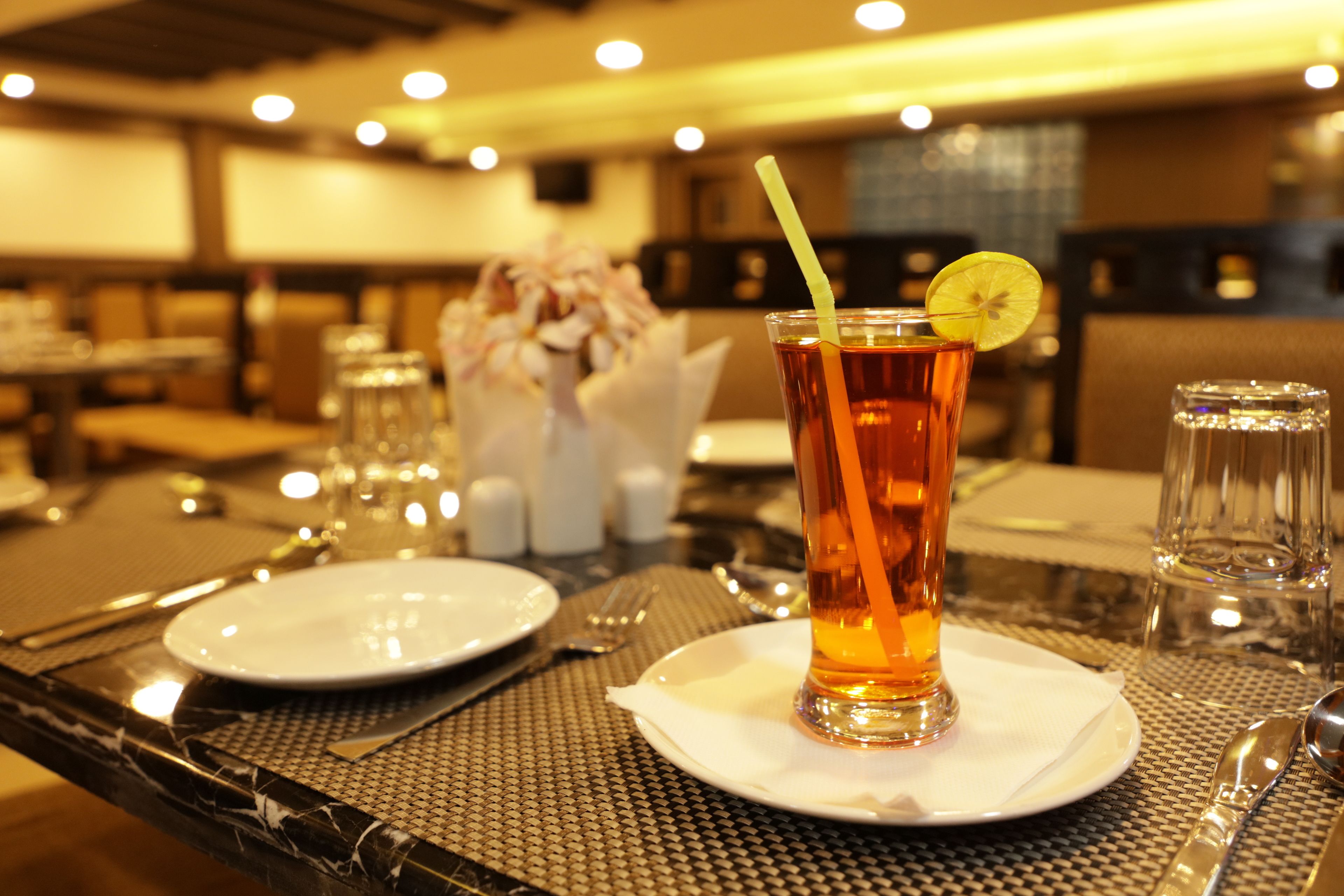 Un restaurante con una mesa lista para comer, incluyendo platos, cubiertos y una taza de té con una rodaja de limón y una pajita.