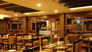 A restaurant with multiple dining tables and chairs, wooden paneled walls, and a sign for 'Crystal Hotel & Restaurant'. - Lee Crysstal (Tirupporur)