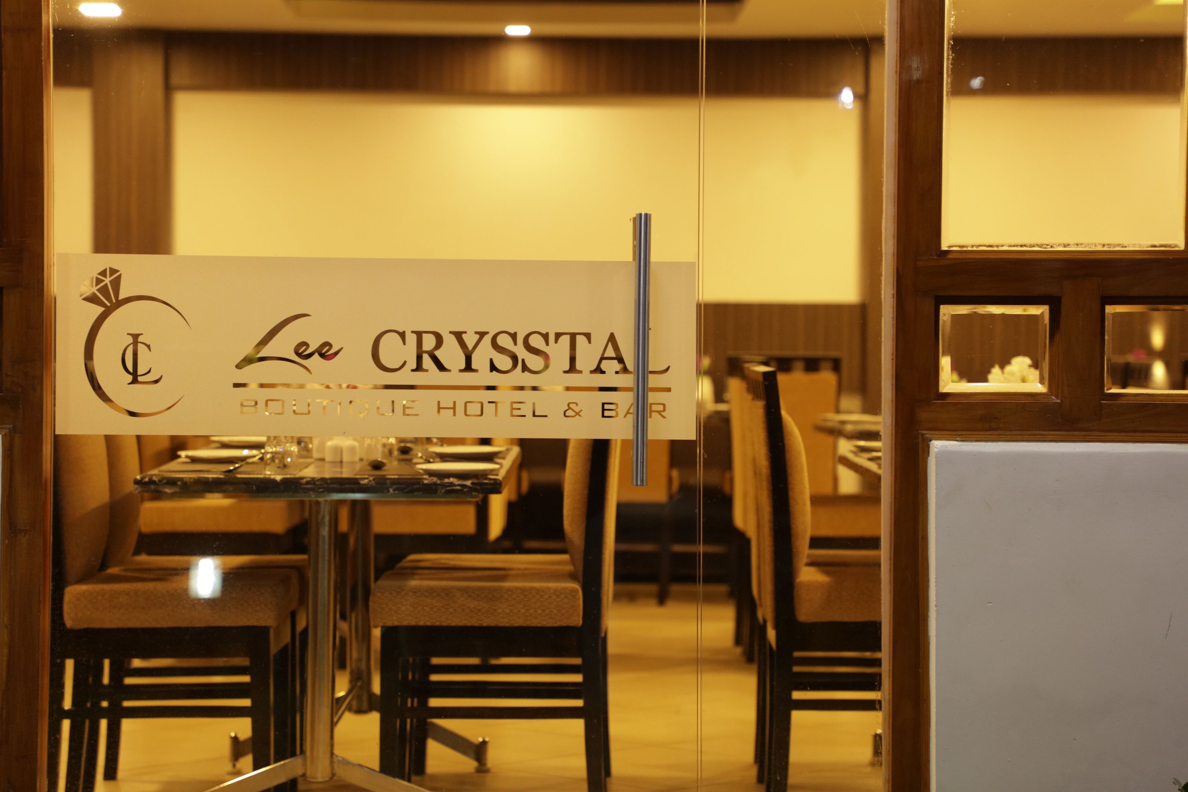 A restaurant interior with tables and chairs, a sign for 'Lee CRYSTAL Boutique Hotel & Bar', and a glass partition.
