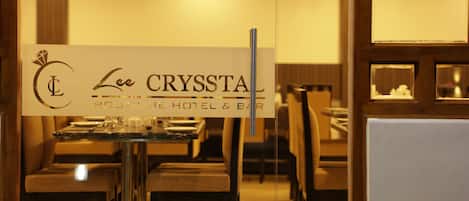 A restaurant interior with tables and chairs, a sign for 'Lee CRYSTAL Boutique Hotel & Bar', and a glass partition.