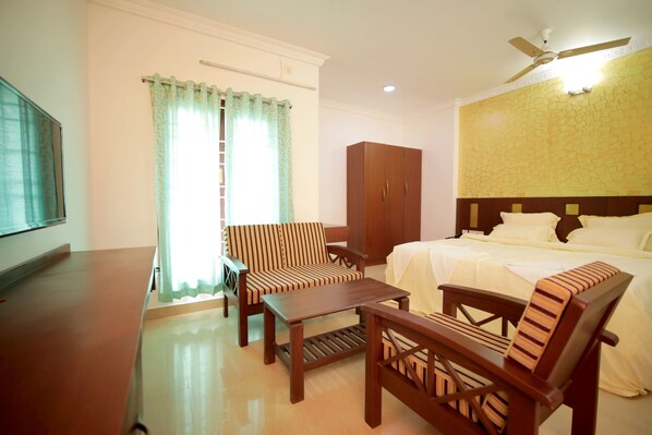 A hotel room with a bed, a wooden chair, a wooden table, a wardrobe, and a ceiling fan.