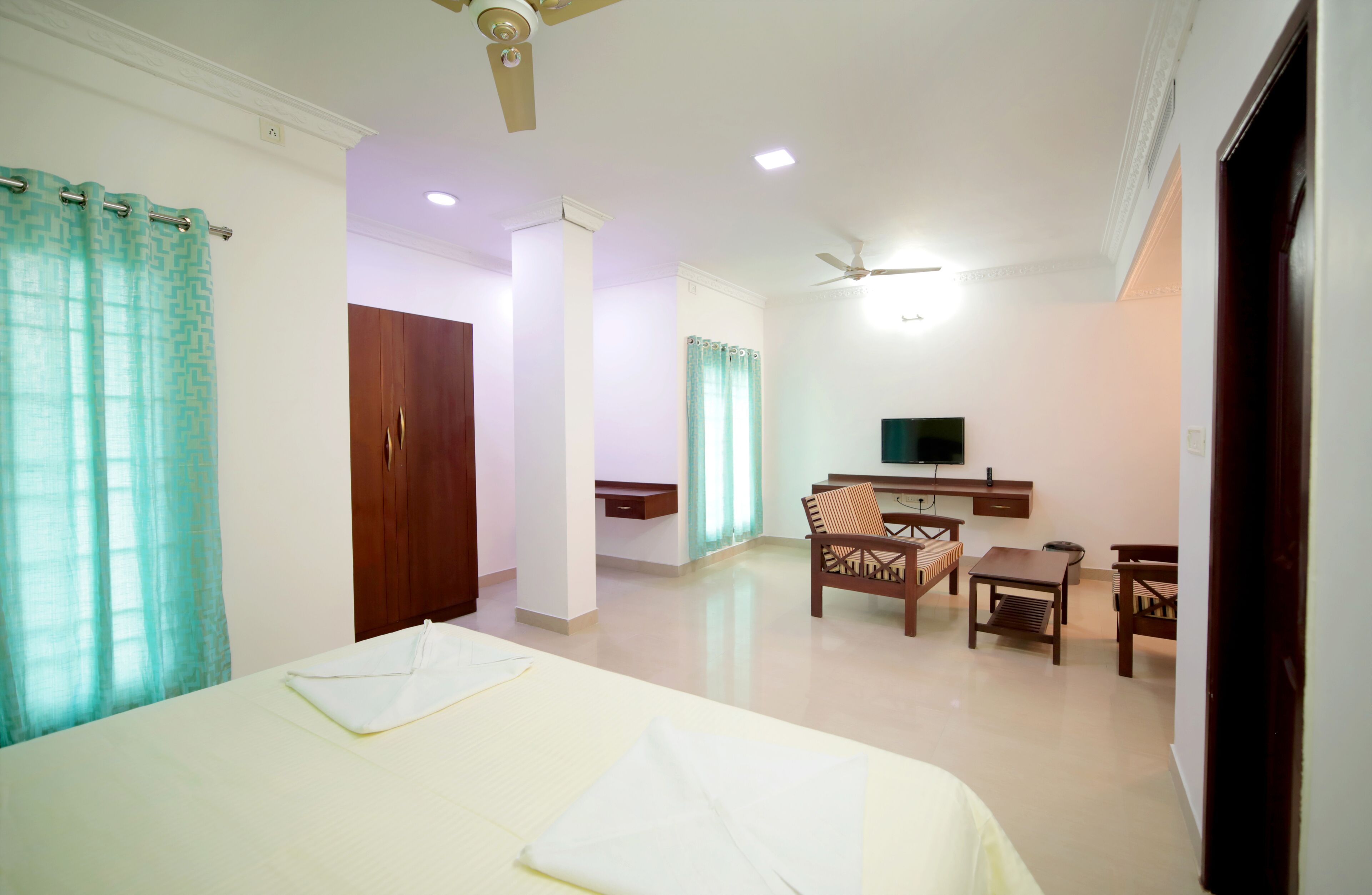 A hotel room with a bed, a desk, a chair, a television, and a ceiling fan.