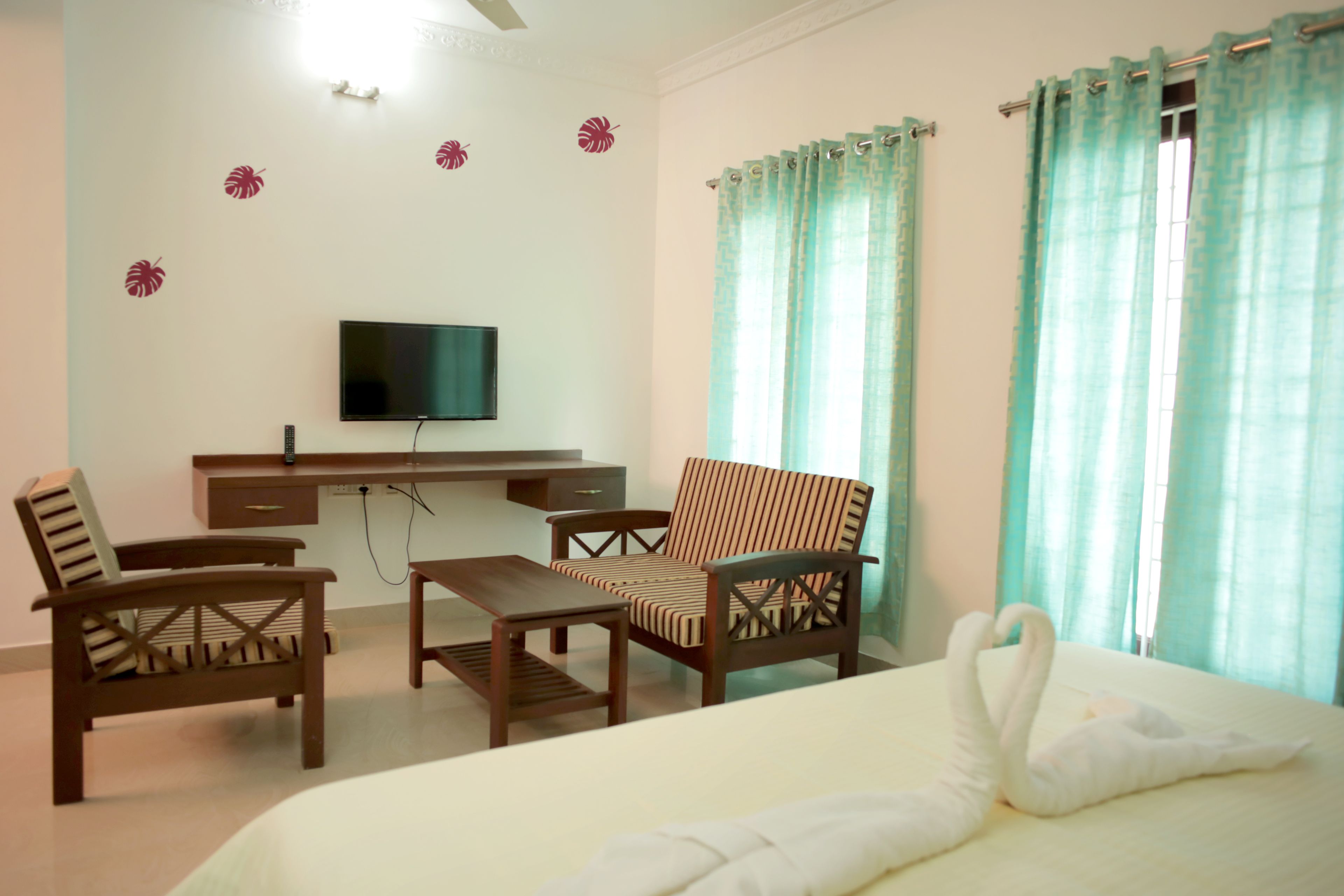 A hotel room with a bed, a TV, a desk with a chair, and a window with curtains.