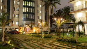 A hotel with a modern design, featuring a central courtyard with palm trees and a red car parked in front. - Lee Crysstal (Tirupporur)