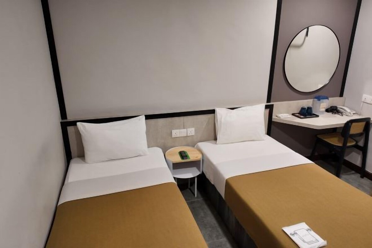A hotel room with two single beds, a small desk with a chair, a telephone, and a mirror on the wall.