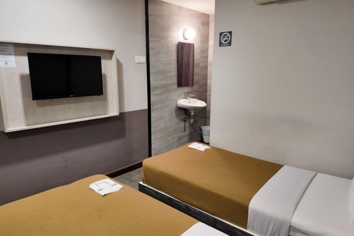 Ett hotellrum med en platt-TV som är monterad på väggen, ett handfat och två sängar med bruna och vita sängkläder.