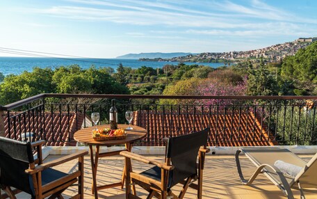 A terrace with a table set for dining, chairs, and a view of the sea and town.