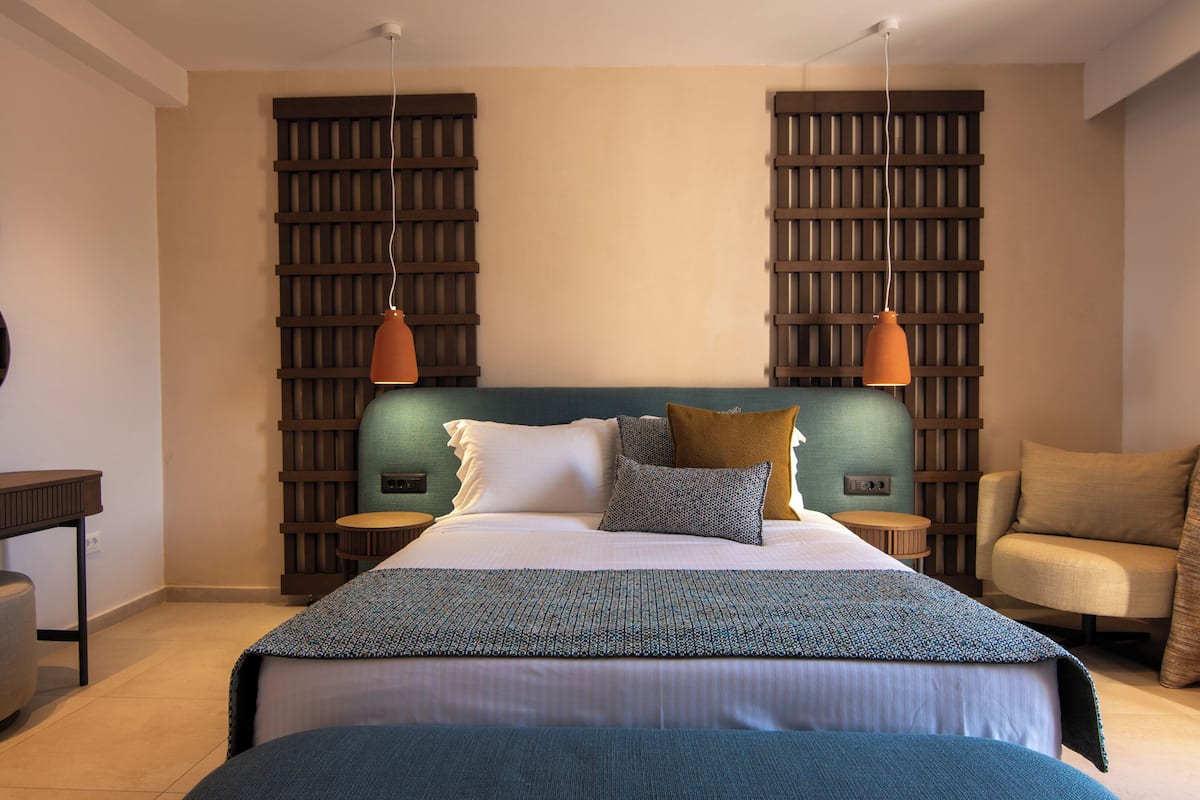 A bedroom with a bed, two nightstands, a chair, and a wall with a wooden panel design.
