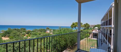 A balcony with a table and chairs, overlooking a coastal landscape with trees and a clear sky.