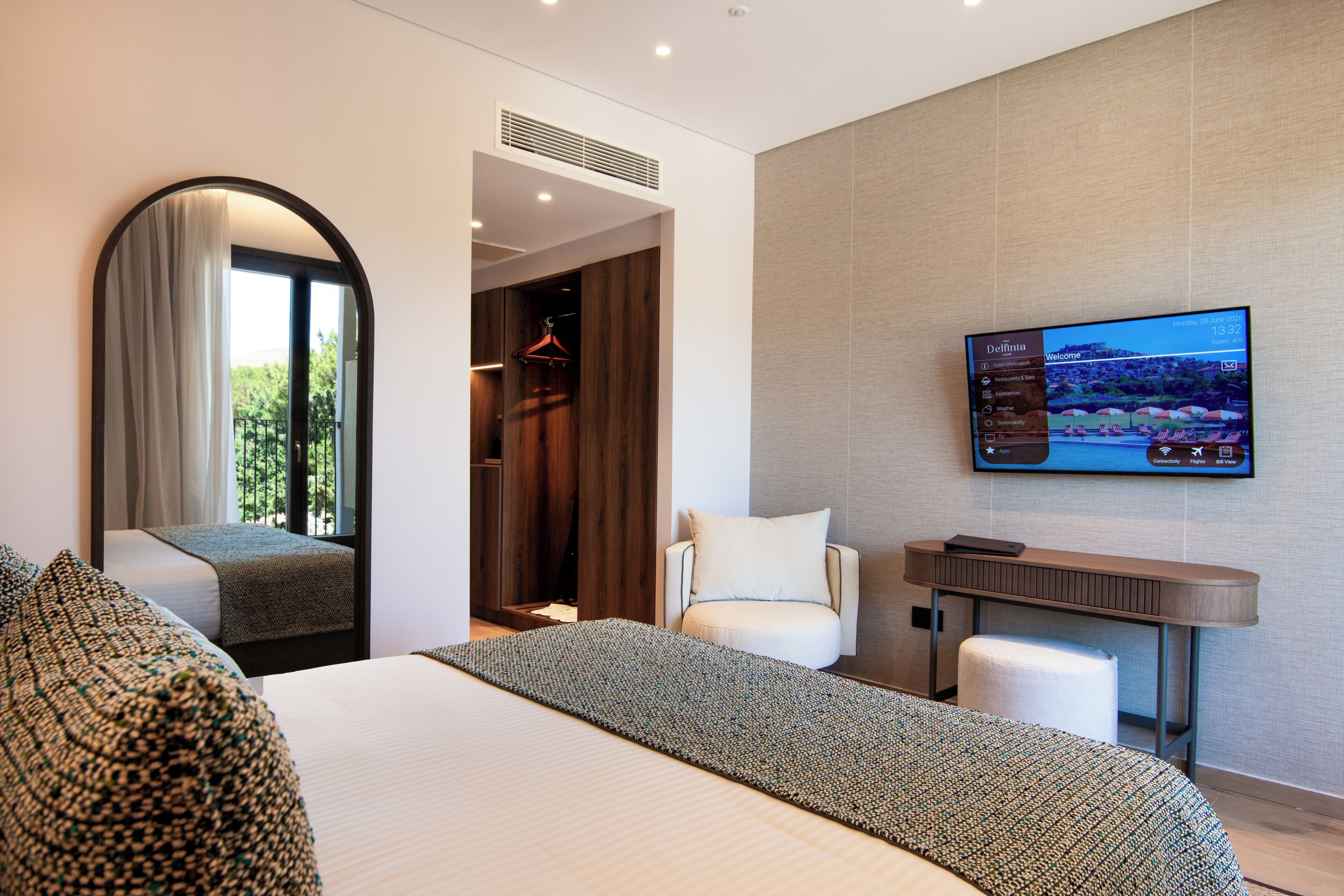 Habitación de hotel moderna con cama, televisor, zona de estar y vistas al exterior.