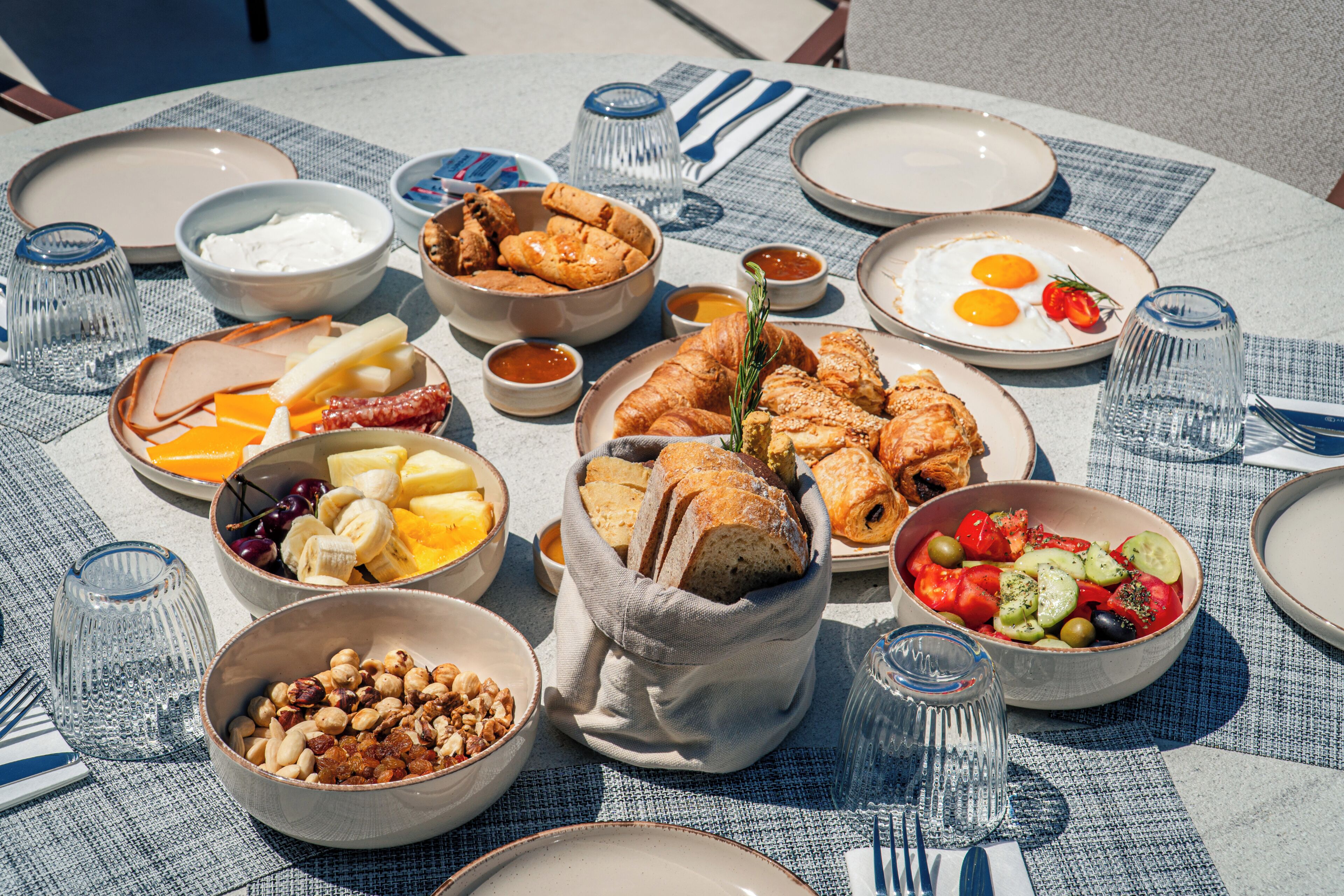 Et rundt bord dækket med forskellige spiser og retter, blandt andet brød, kager og frugt.