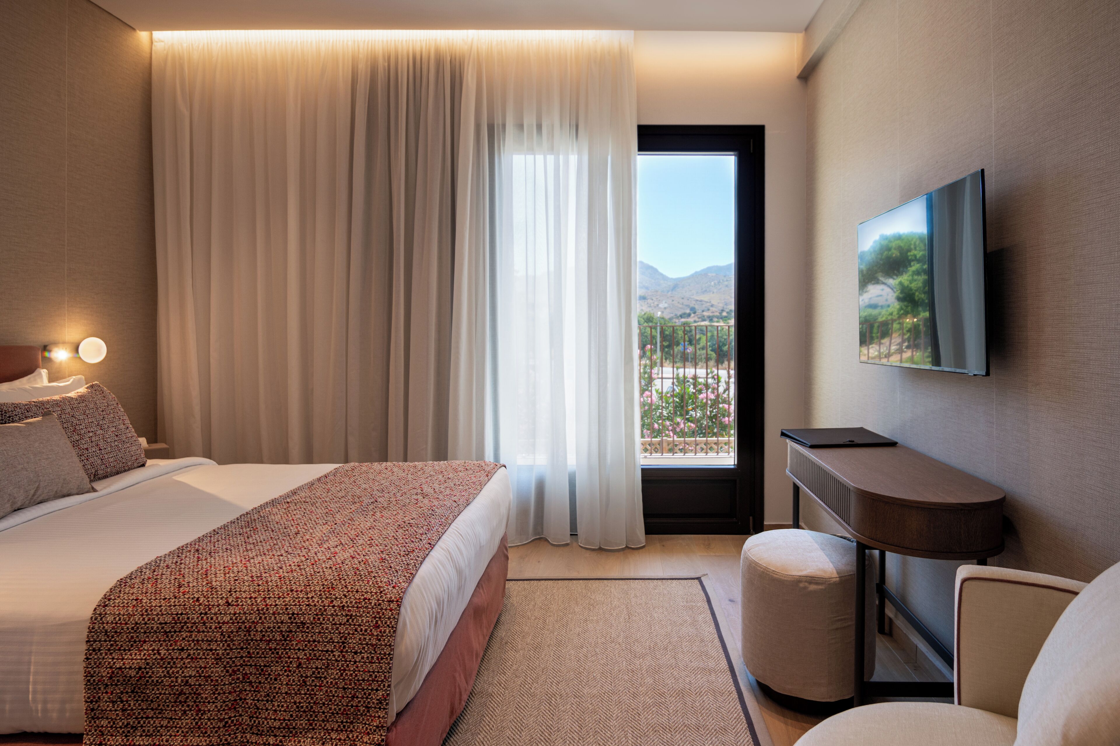 A hotel room with a bed, a desk, a chair, a television, and a view of the outdoors.