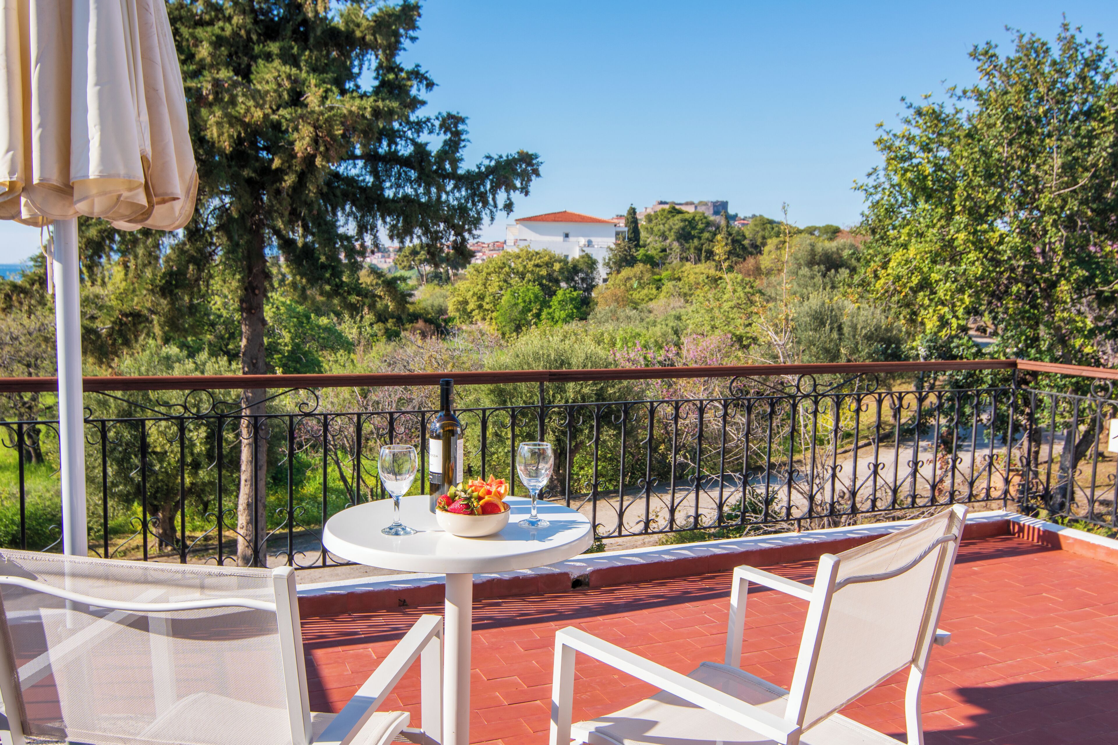 A balcony with a table set for two, a bottle, and a bowl of fruit.