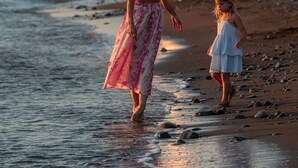 Escena de playa con una mujer y un niño caminando por la orilla.