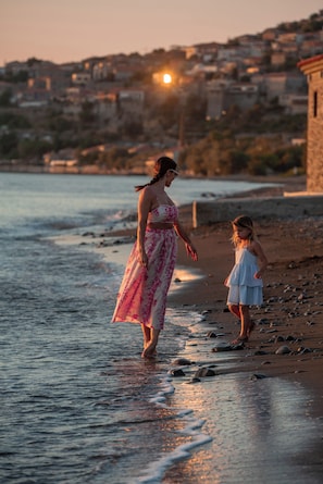 A beach scene with a woman and a child walking along the shore. - Hotel Delfinia (Lesvos)