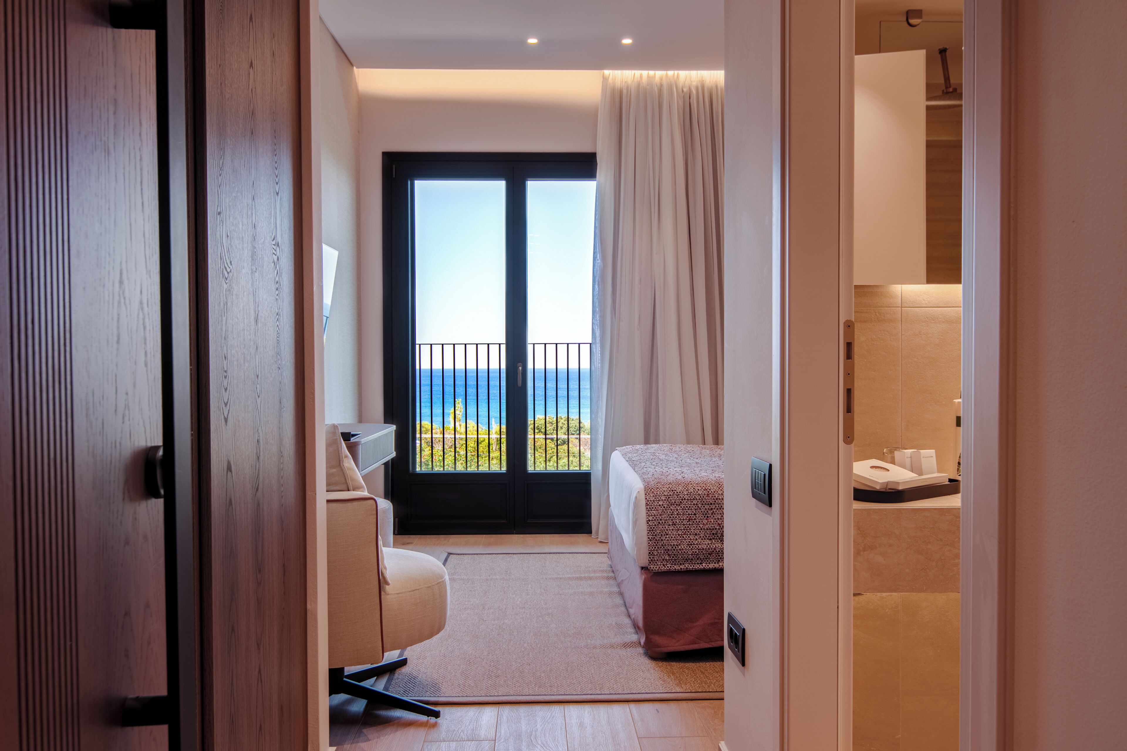 A hotel room with a bed, a desk, a chair, a bathroom, and a balcony with a view.