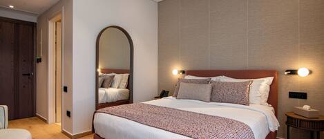 Habitación de hotel con una cama grande, una mesita de noche con una lámpara, un espejo y una puerta que da a otra habitación.