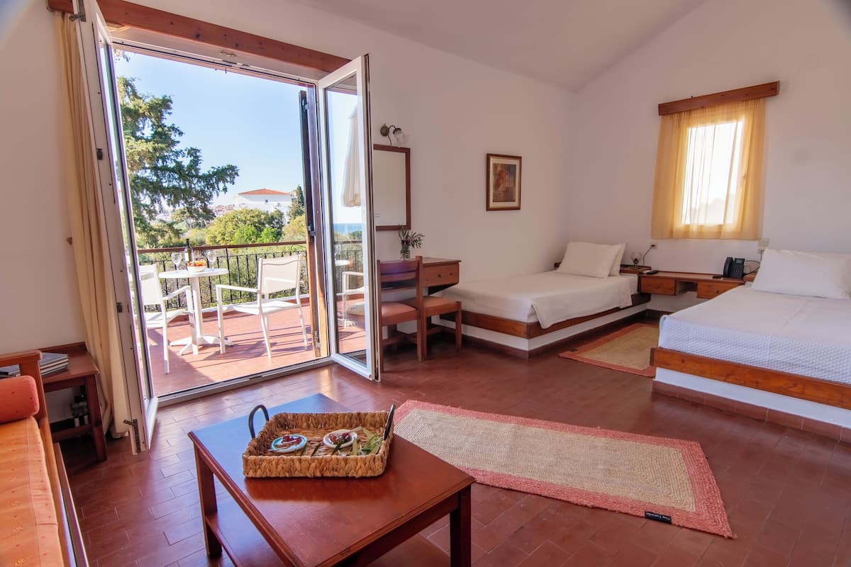A bedroom with a bed, a desk, a chair, a small table with a tray, and a balcony with a table and chairs.