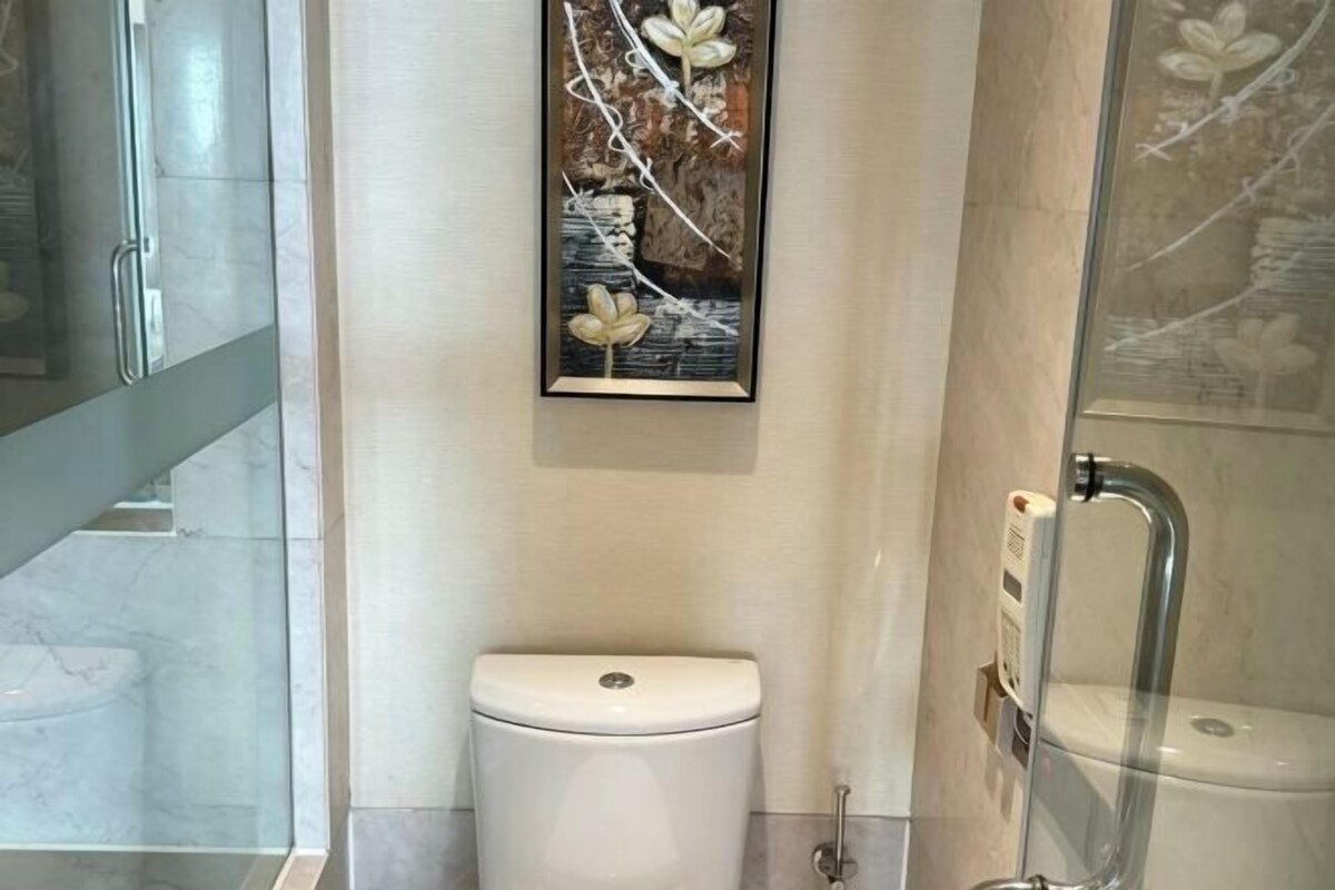 Un baño moderno con inodoro, cabina de ducha de vidrio y una obra de arte en la pared.
